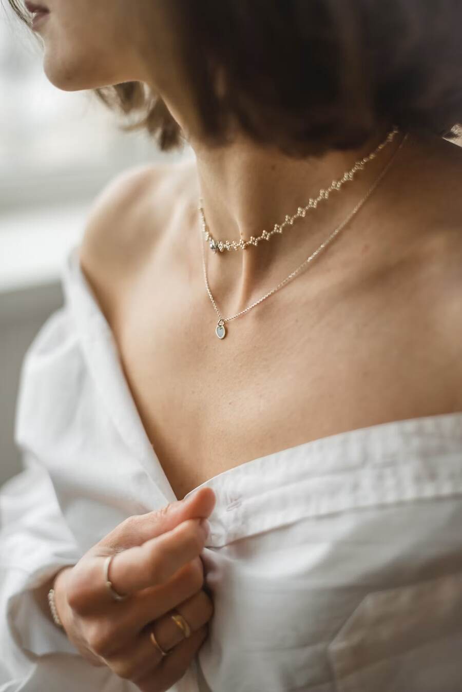 Layered fine chain necklaces worn with an open white shirt